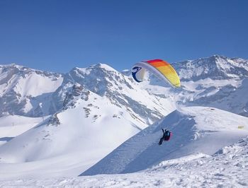 Person paragliding over snowcapped mountain against clear blue sky