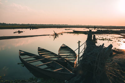 Fishing boats moored at lake against sky during sunset