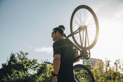 Male athlete carrying bicycle on shoulder against sky on sunny day