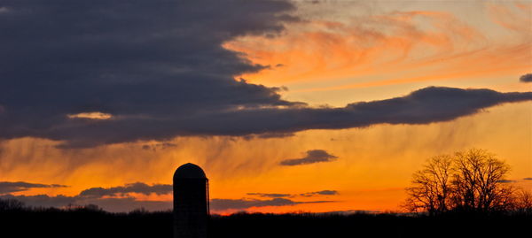 Silhouette silo on field against orange cloudy sky during sunset