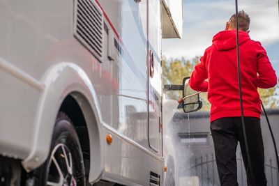 Rear view of man cleaning car with hose