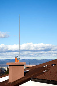 A chimney with a lightning rod against blue sky with mountains in the background