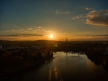 Scenic view of river by buildings against sky during sunset