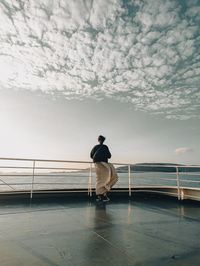 Rear view of man walking on bridge against sky during sunset