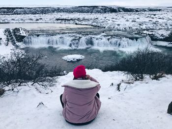 Rear view of person looking at waterfall while sitting on snow covered field