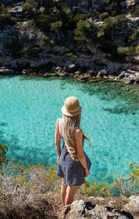 Rear view of woman sitting on rock by lake