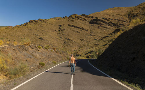 Rear view of shirtless man walking on road against mountain range