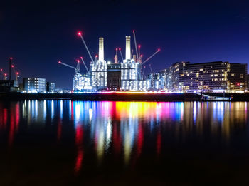 Illuminated city by river against sky at night