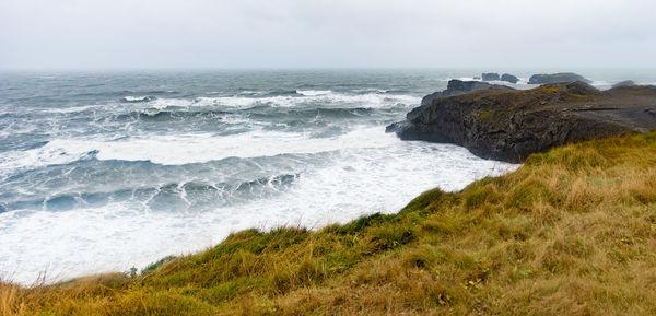 Waves splashing on rocks at shore against sky