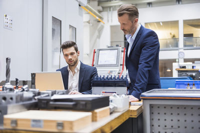 Two men at table in factory using laptop