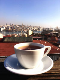 Close-up of coffee cup on table against buildings in city