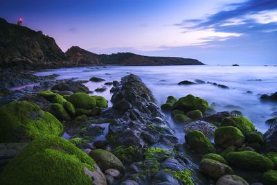 Rocks on beach against sky during sunset