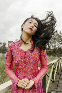 Portrait of young woman tossing hair against sky