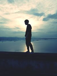 Silhouette man standing on retaining wall against sea