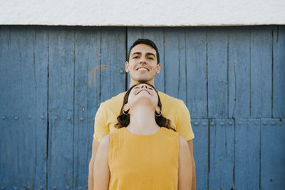 Young woman leaning on smiling man in front of wall