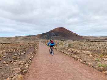 Rear view of man riding on bicycle on dirt road 