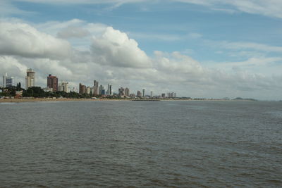 View of city at waterfront against cloudy sky