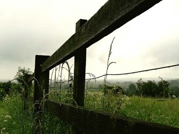 Fence on grassy field against cloudy sky