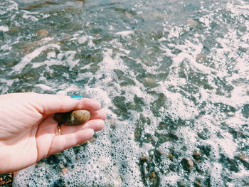 Cropped hand of woman holding stone against sea