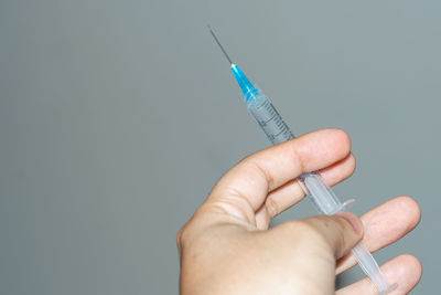 Cropped hand holding syringe against blue background