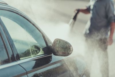 Midsection of man washing car on road