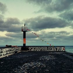 Lighthouse by sea against dramatic sky