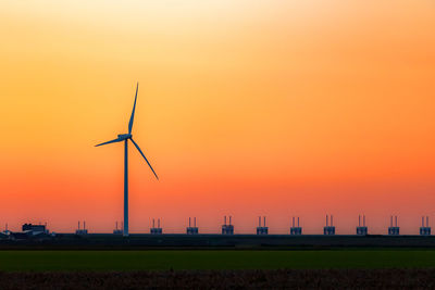 Silhouette wind turbines on field against orange sky