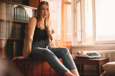 Young woman sitting by bookshelf