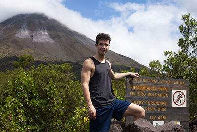 Smiling young man standing by sign against volcano