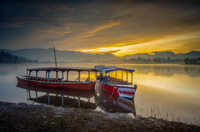 Boat moored on lake against sky during sunrise