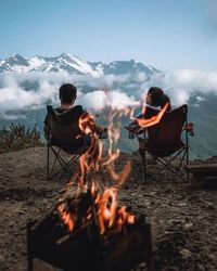 Rear view of men sitting on barbecue against sky