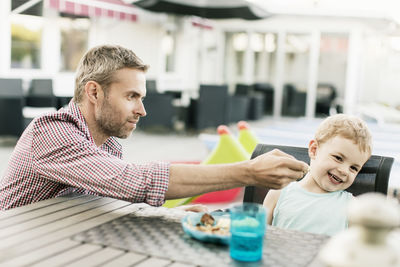 Smiling boy refusing to eat food offered by father at restaurant