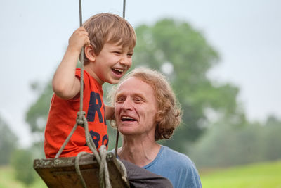 Happy grandfather and grandson with rope swing in public park