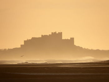 Scenic view of sea by castle against clear sky during sunrise