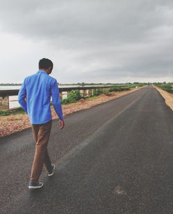 Rear view of man walking on road against sky