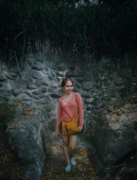 Portrait of young woman standing against stone wall