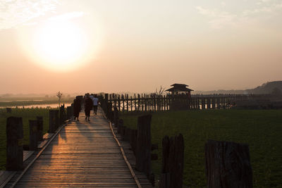 People walking on pier over lake against sky during sunset