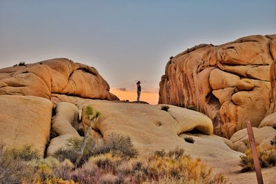 Side view of woman standing on rock formations against sky