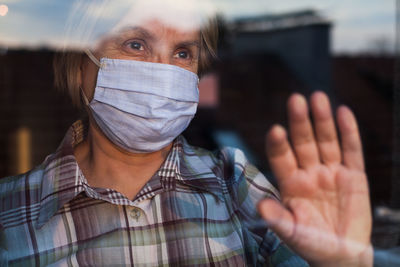 Senior woman wearing mask standing by window at home