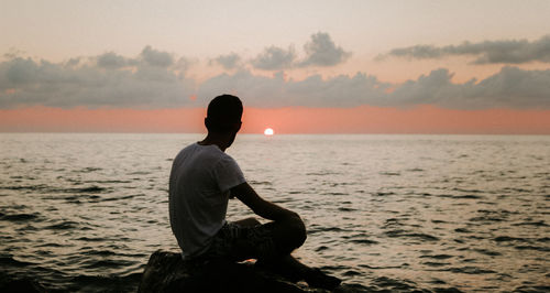 Man looking at sea against sky during sunset