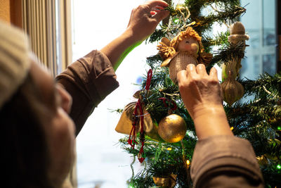 A senior woman hands hang christmas baubles, lights and spheres