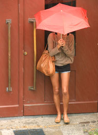 Woman holding umbrella standing against closed door of building