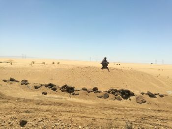 Low angle view of man crouching in desert against clear sky during sunny day