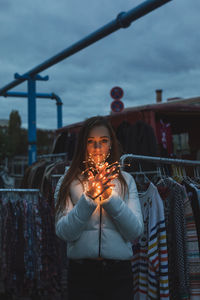Portrait of young woman holding illuminated lighting equipment at clothes market