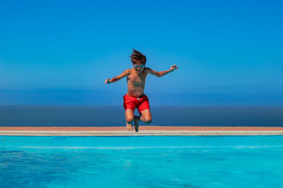 Full length of woman jumping at beach against blue sky