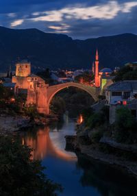 Illuminated bridge over river against cloudy sky