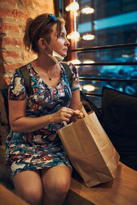 Young woman sitting in coffee shop at store front after shopping in the city center in the evening