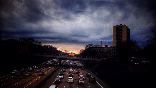 Road passing through city against cloudy sky