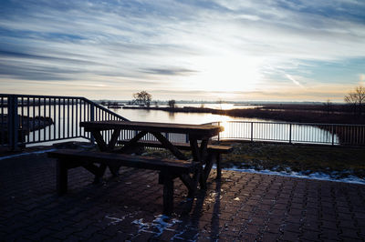 Empty bench on table against sky during sunset