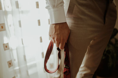 Midsection of man holding belt while standing at home